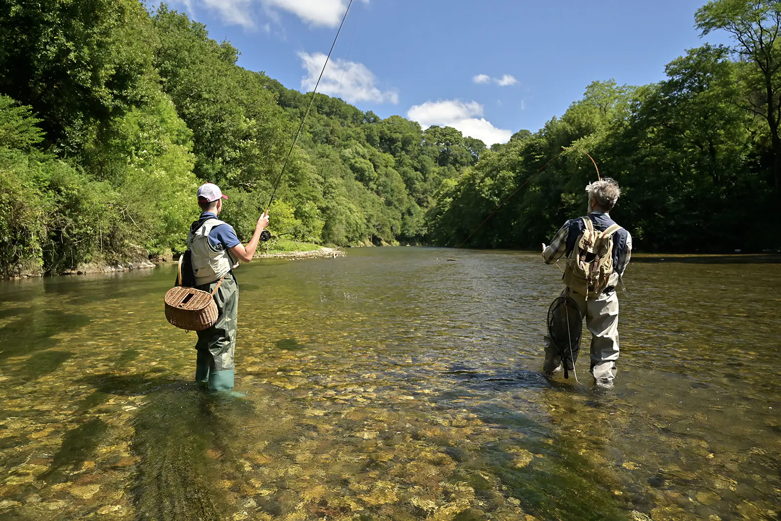 Two people stand in the Little Tennessee River with their backs turned casting fly fishing lines into the water.
