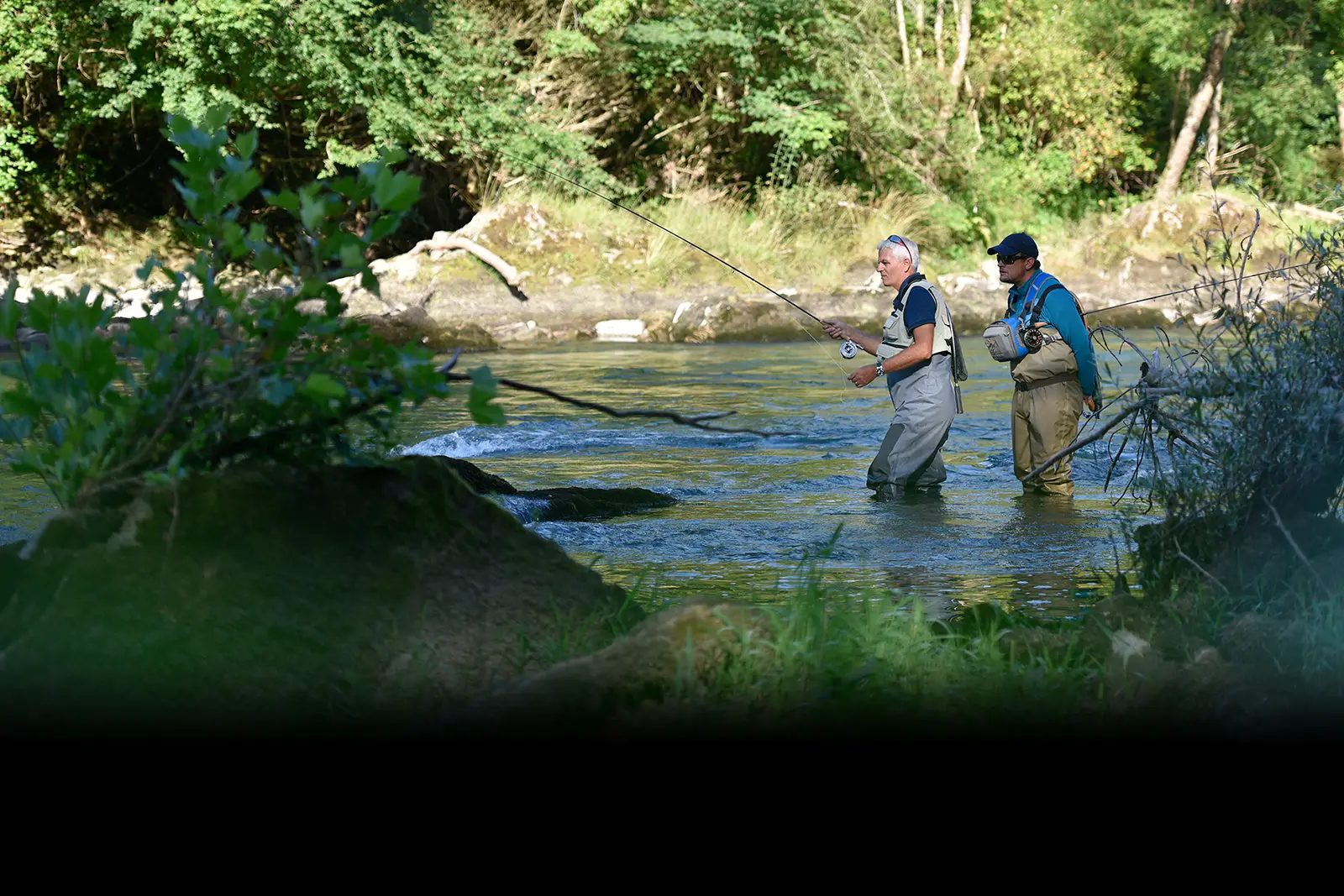 A fly fishing guide standing behind and angler in a river teaching him how to fly fish.