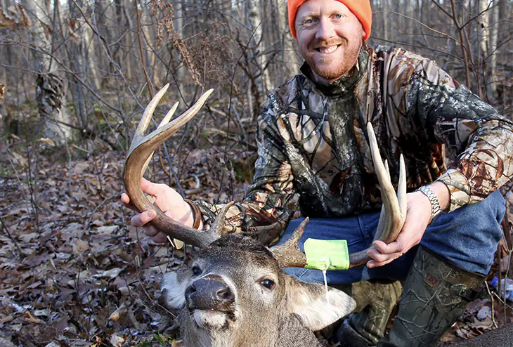 A man wearing camouflage gear posing with a deer he hunted in a forest in North Carolina.
